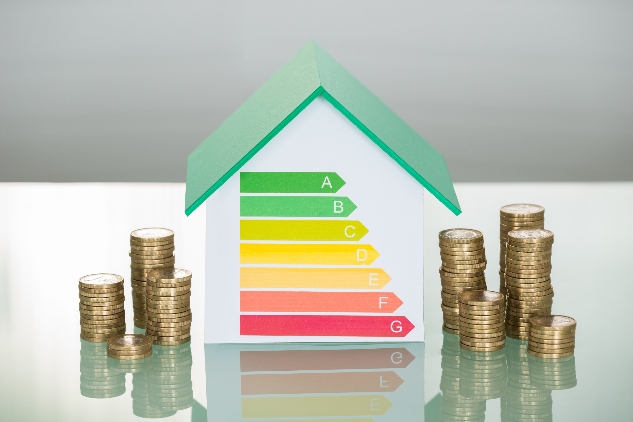 Pile de pièces et maquette de maison affichant le taux d'efficacité énergétique sur le bureau